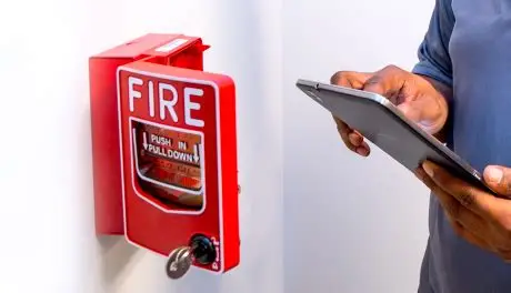 Technician checking a fire alarm pull station with a tablet